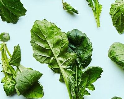 Fresh green leafy vegetables on a light blue background.